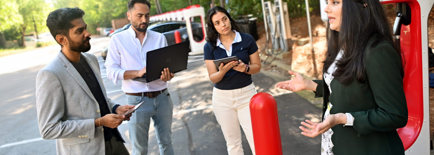 Leila Hajibabai talking with three students while standing in front of an electric car charging station.